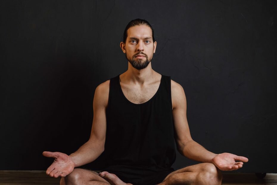 a bearded man in black tank top sitting while meditating